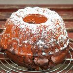 Ciambellone appena sfornato su un tavolo con ingredienti e utensili da cucina.