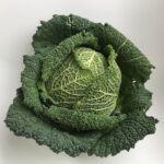 Cavolo nero fresco su un tagliere con utensili da cucina e un ricettario aperto.