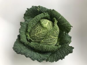 Cavolo nero fresco su un tagliere con utensili da cucina e un ricettario aperto.