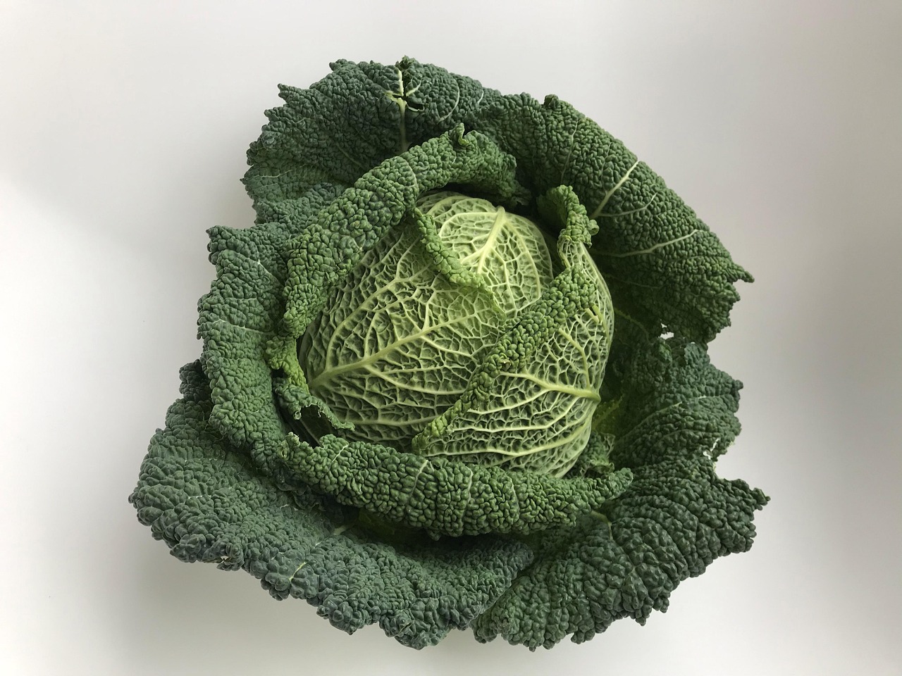 Cavolo nero fresco su un tagliere con utensili da cucina e un ricettario aperto.